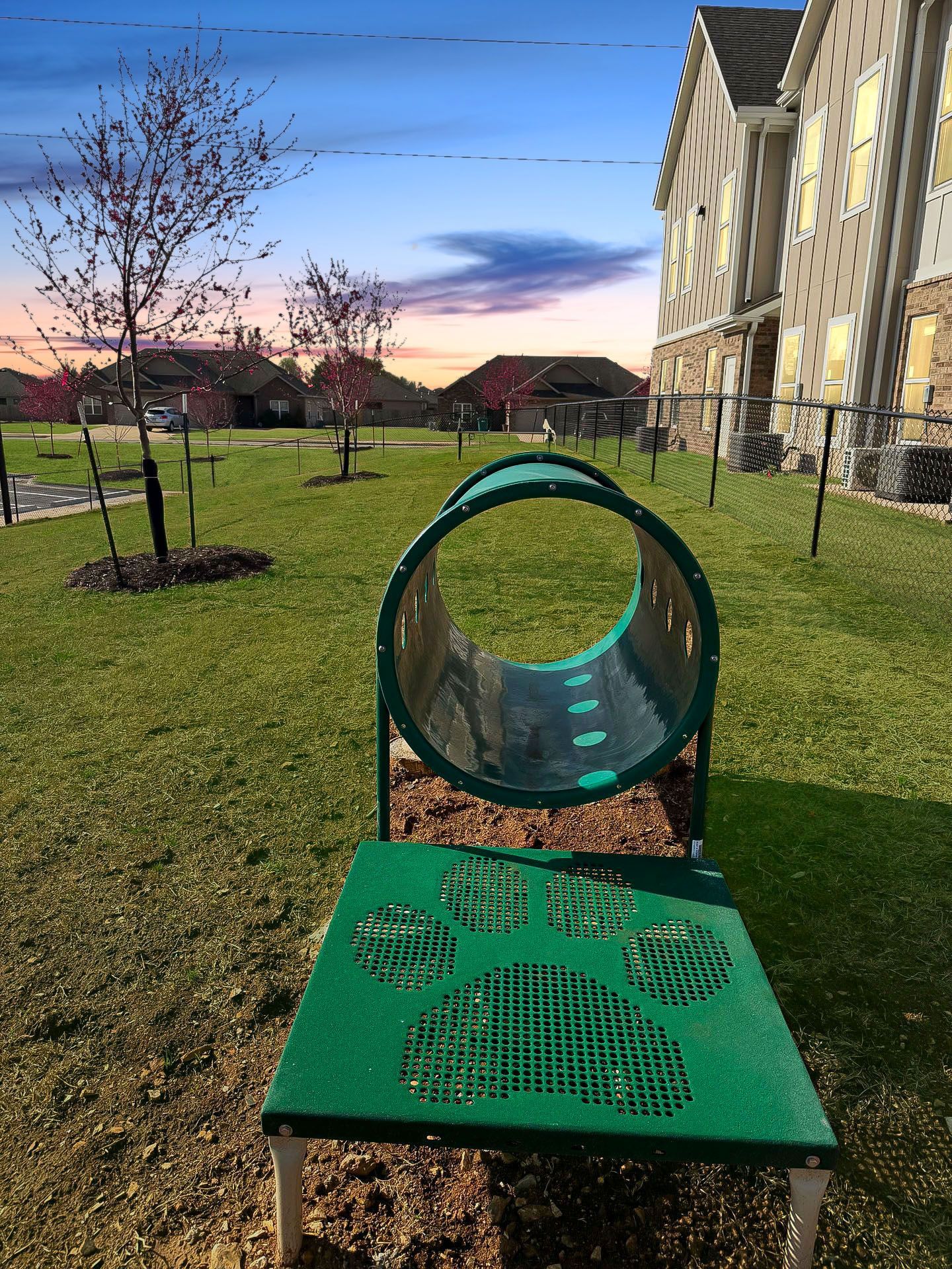 A green dog tunnel in a park with a building in the background.