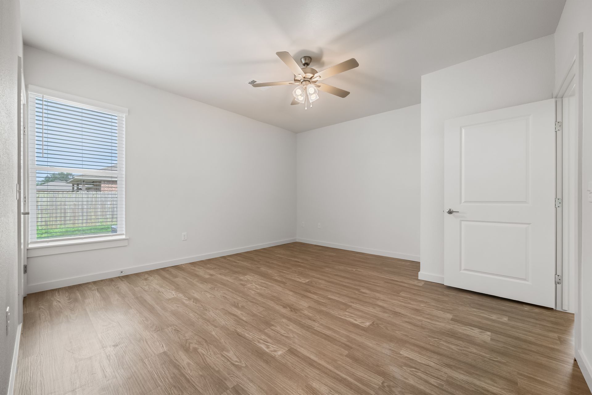 An empty bedroom with hardwood floors and a ceiling fan.