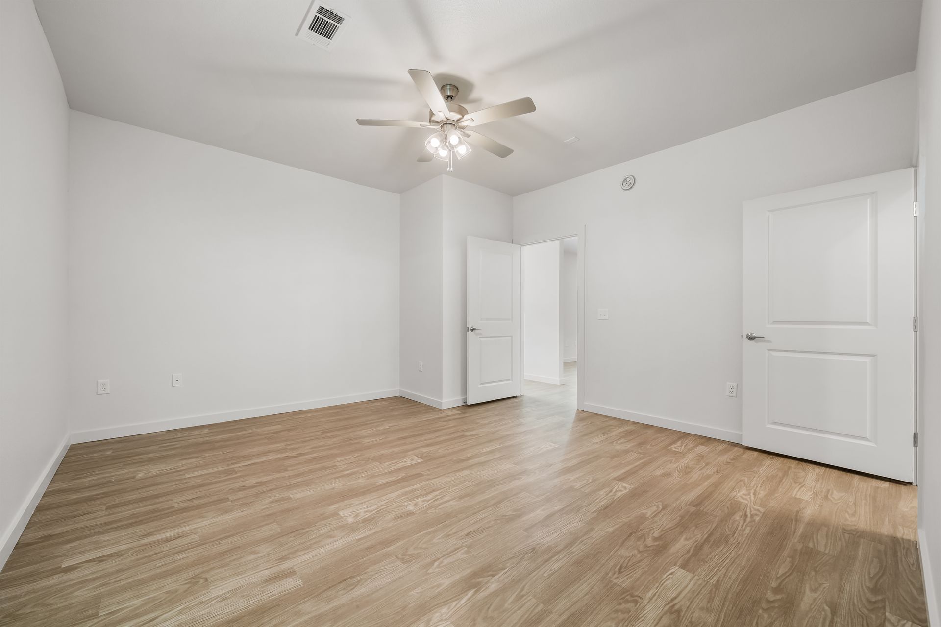 An empty bedroom with hardwood floors and a ceiling fan.