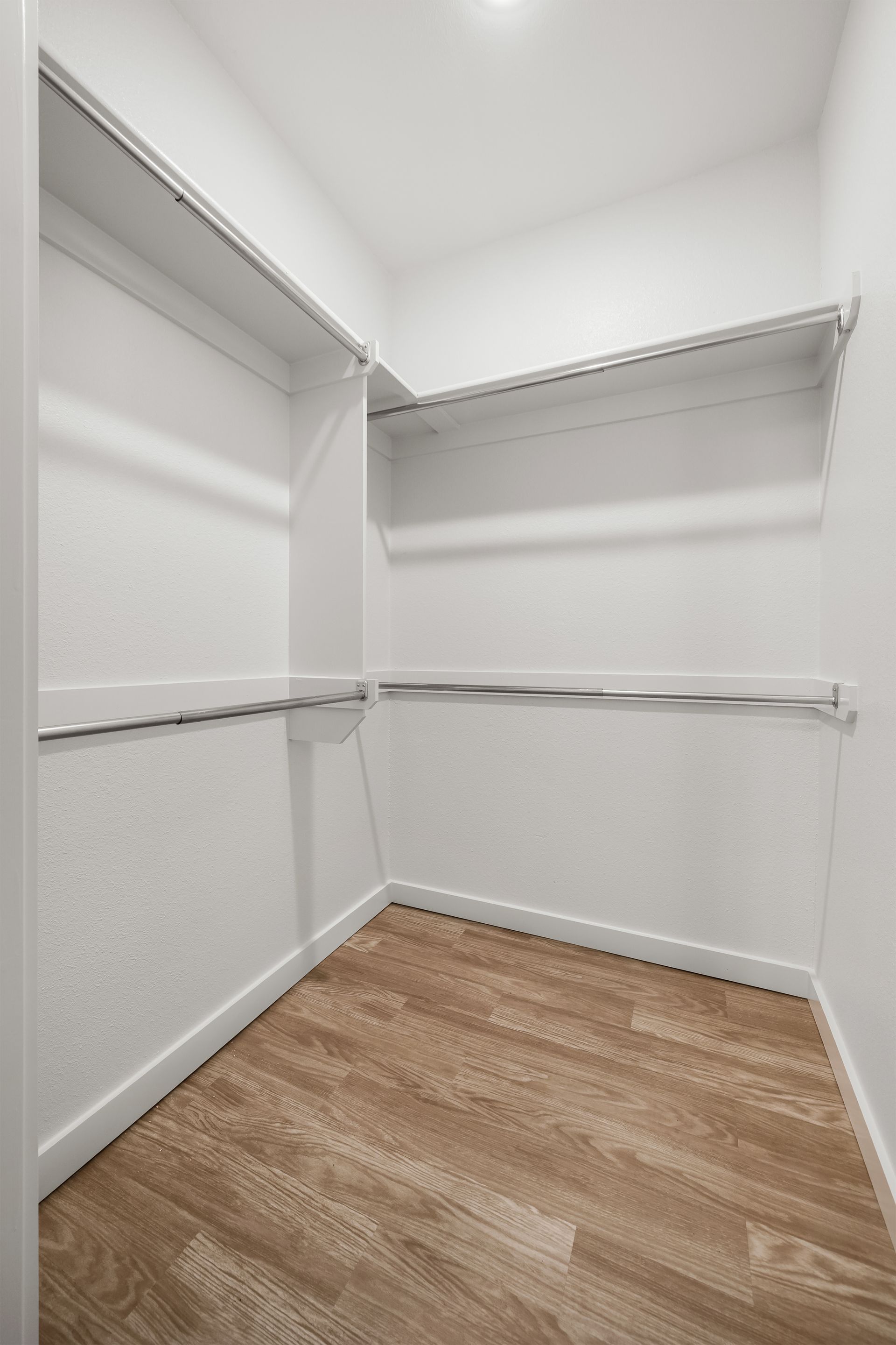 An empty walk in closet with hardwood floors and white walls.