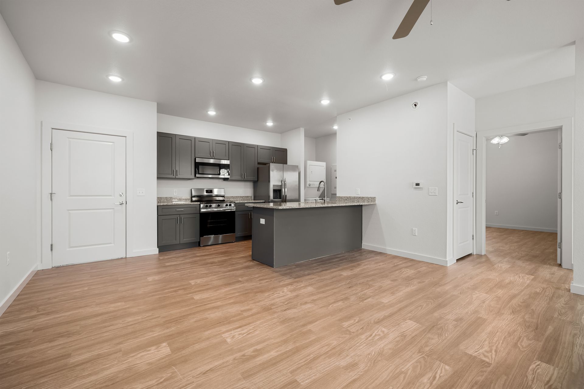 An empty apartment with a kitchen and a ceiling fan.