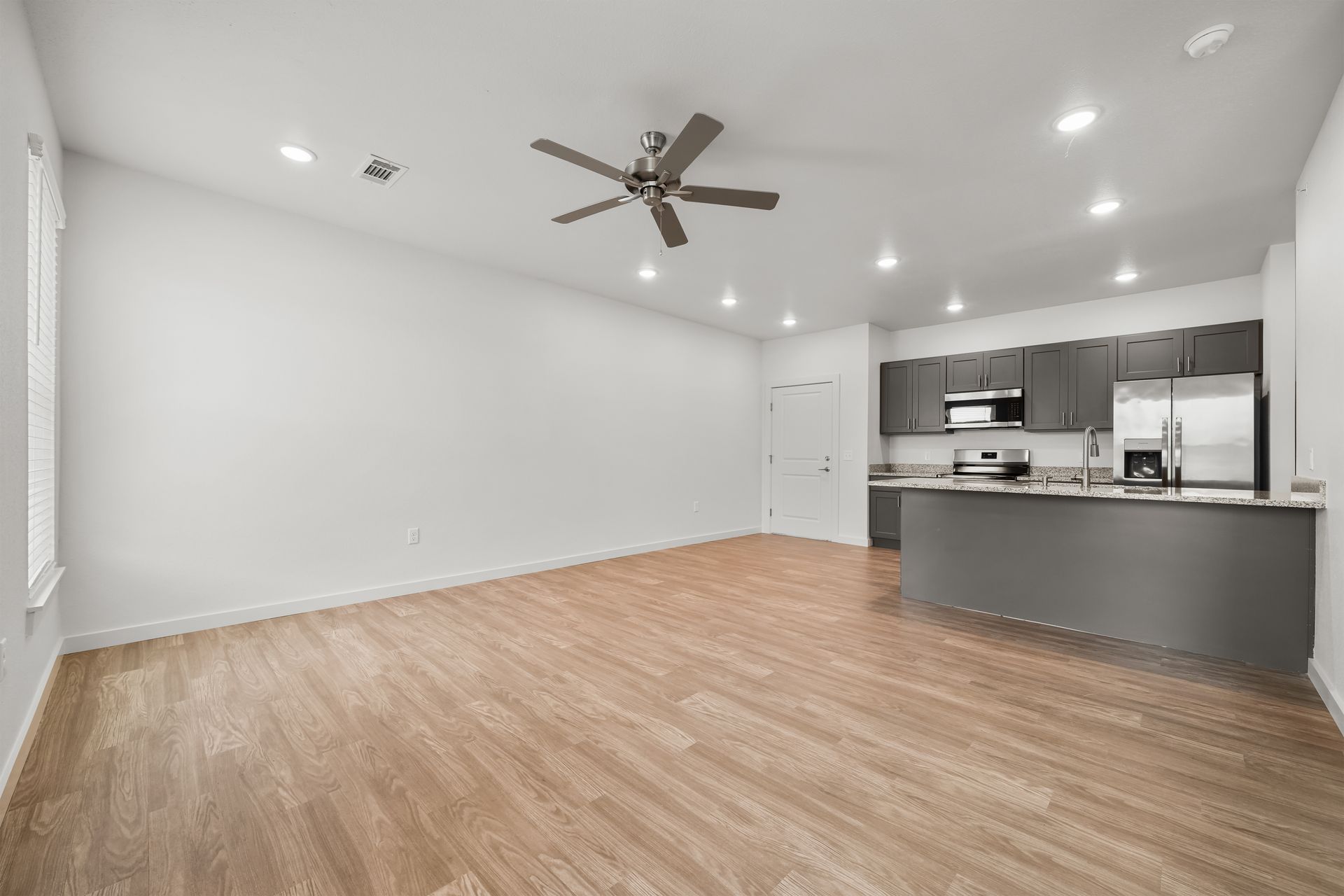 An empty living room with hardwood floors and a ceiling fan.