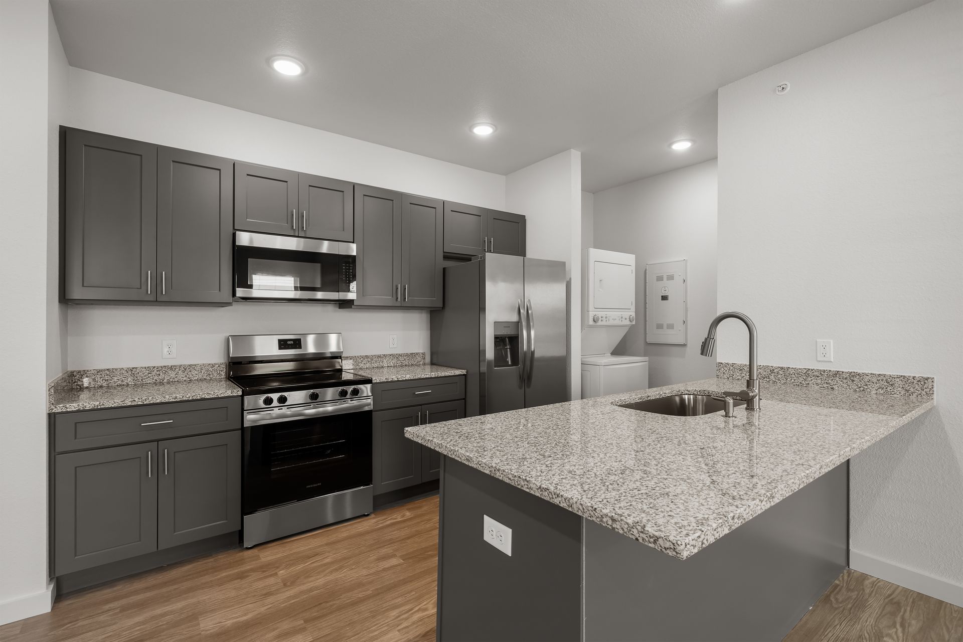 A kitchen with granite counter tops , stainless steel appliances , and gray cabinets.