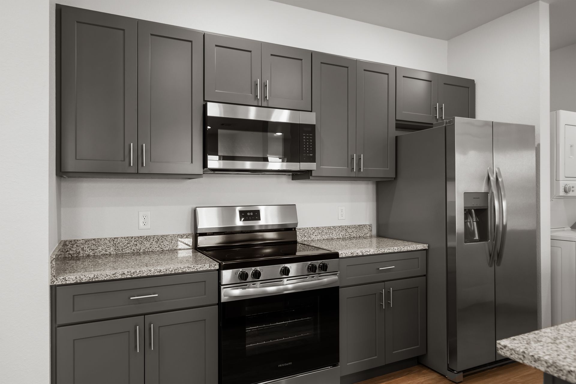 A kitchen with gray cabinets , a stove , a refrigerator , and a microwave.