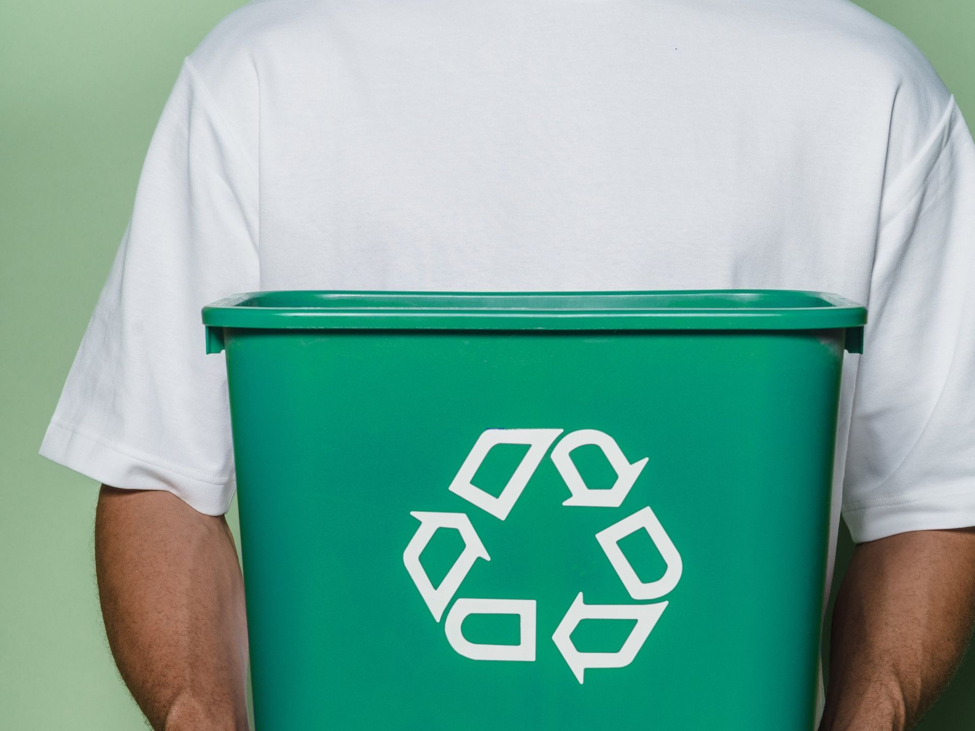 Un homme tient un bac de recyclage vert derrière son dos.