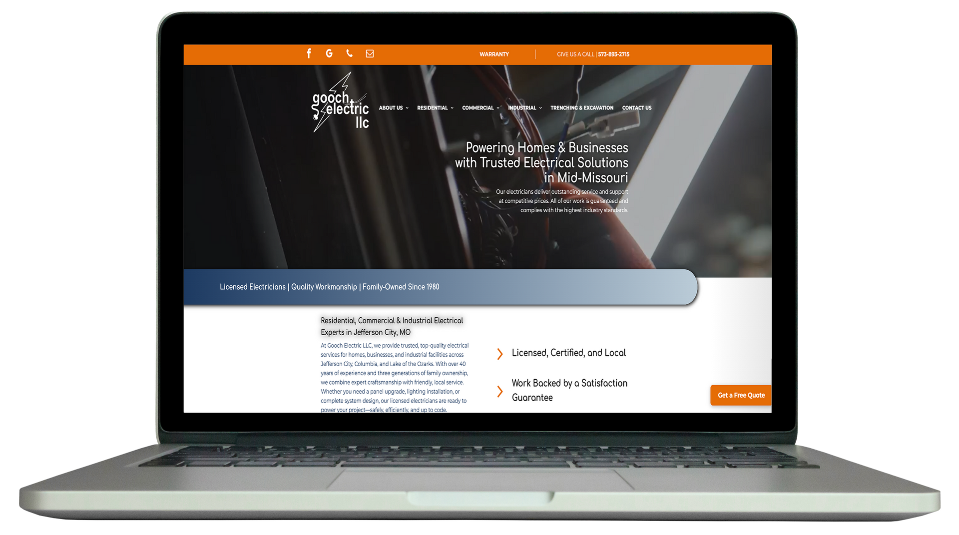 A silver laptop displaying a business website featuring a dark, blurred background and orange accents.