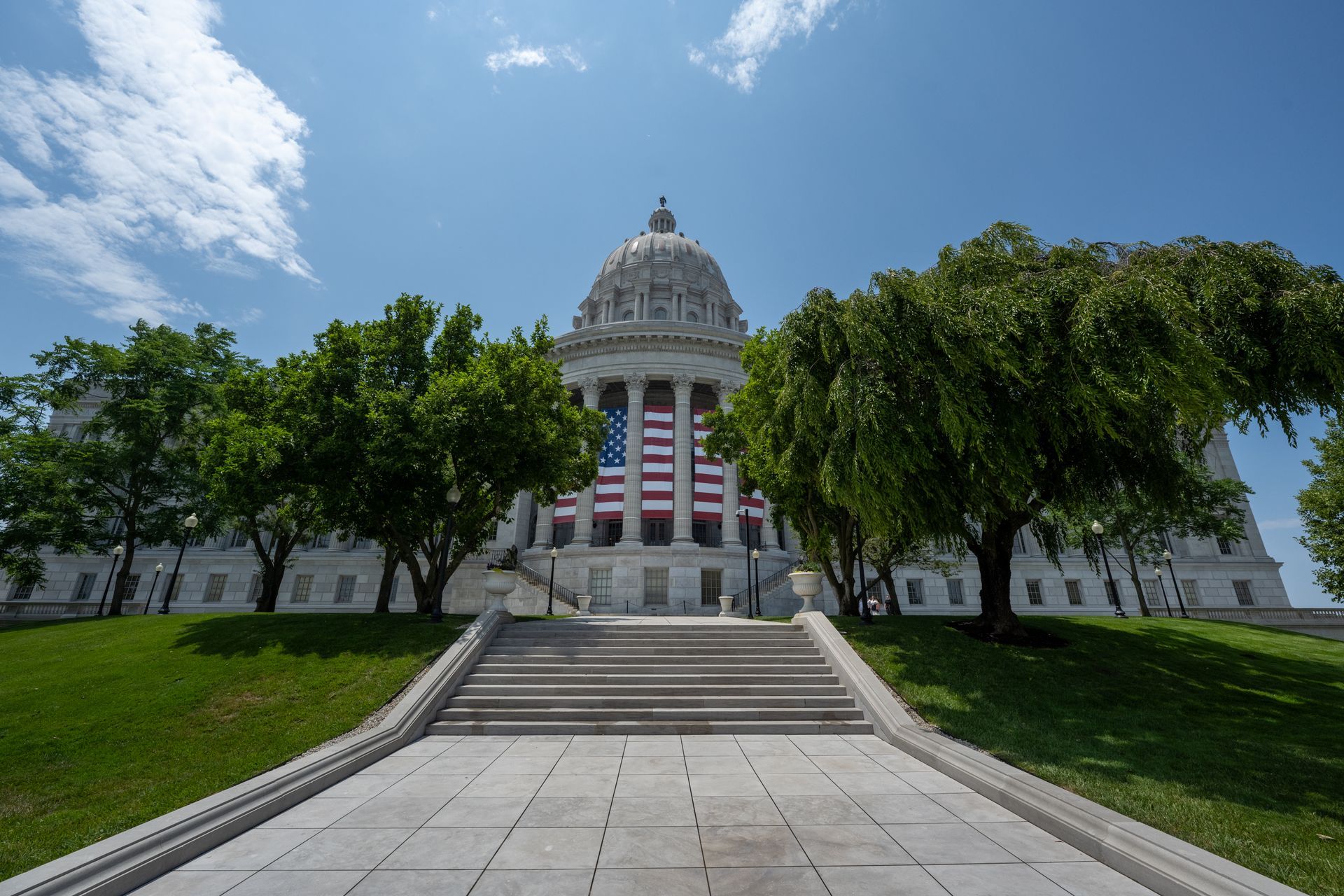 A wide, upward-facing shot of the Missouri State Capitol building with a large American flag draped under its central dome.
