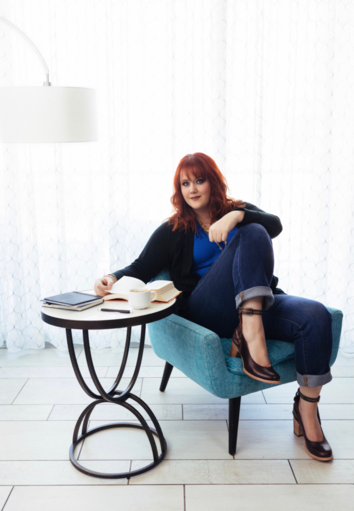 Woman with hand on chin, wearing beaded jewelry, smiling, against a dark backdrop.