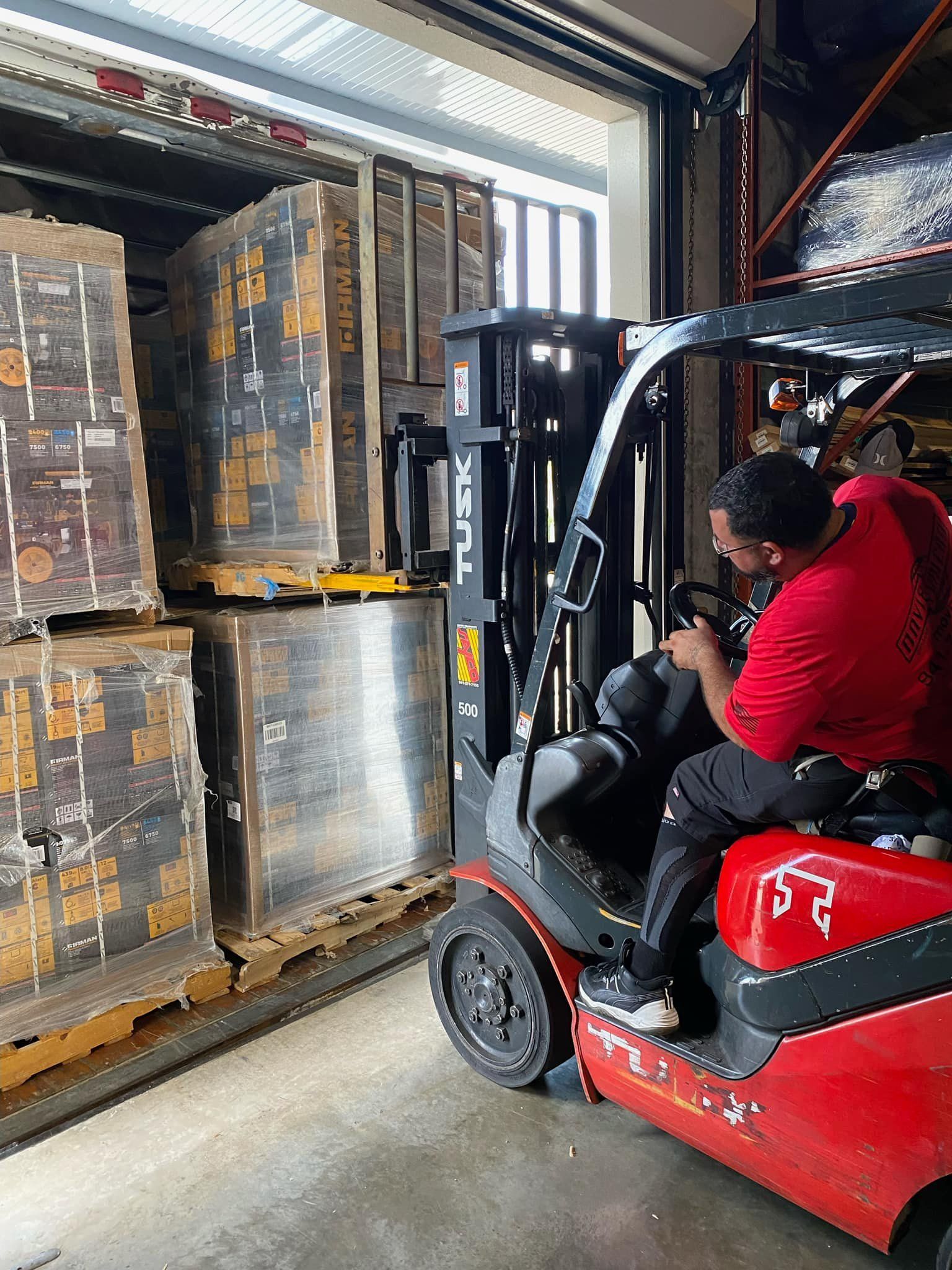 Forklift loading pallets of goods inside a warehouse. Person in red operating the forklift.