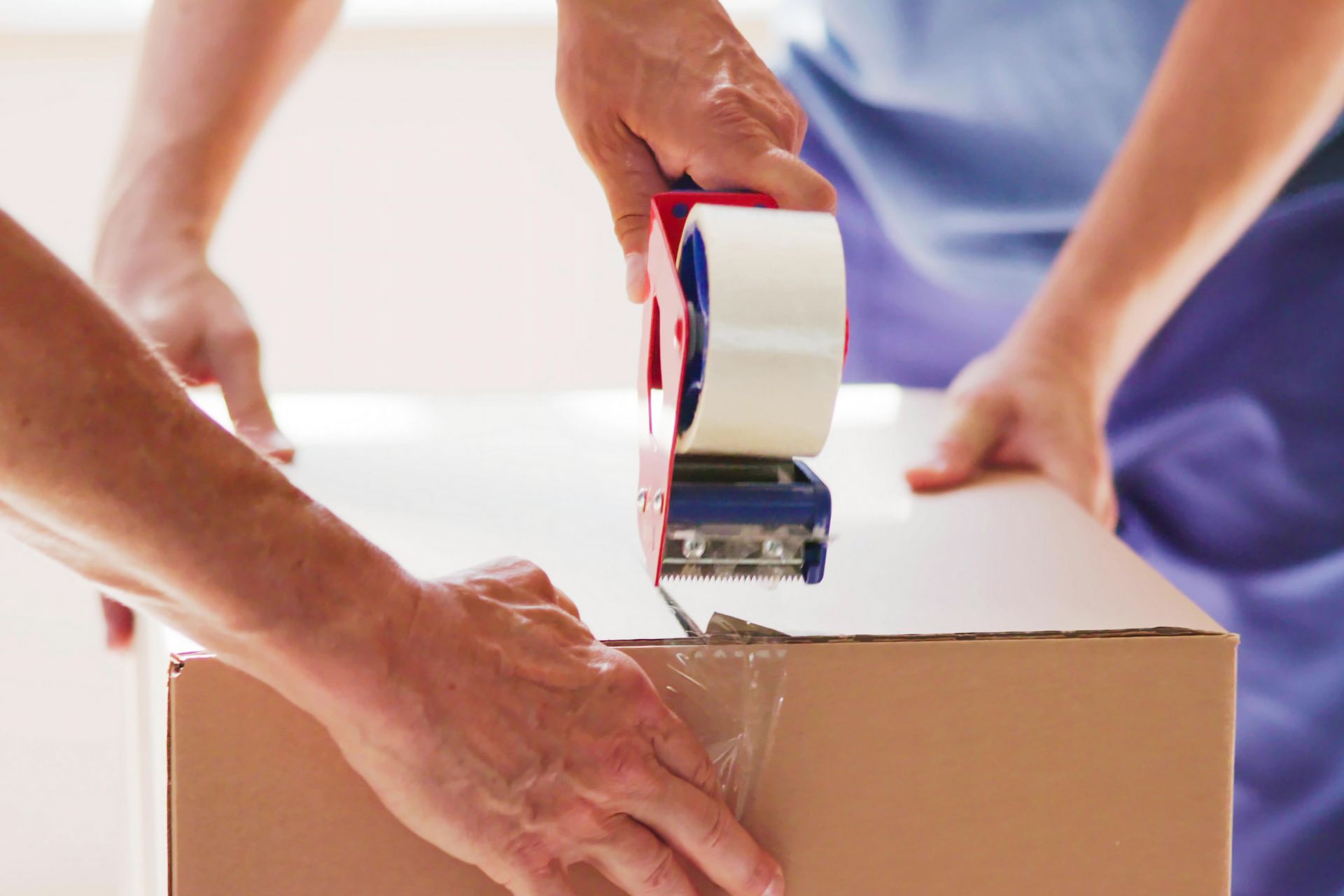 Two sets of hands work together to seal a cardboard box with a tape dispenser.