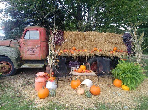 A photo of one of Flowers Pumpkin Farm's photo areas; an old red truck pulls a wagon with straw bales, pumpkins, gourds, and corn stocks,