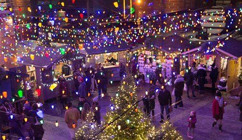 An ariel shot of Christmas shoppers browsing outdoor vendor booths under a canopy of Christmas lights