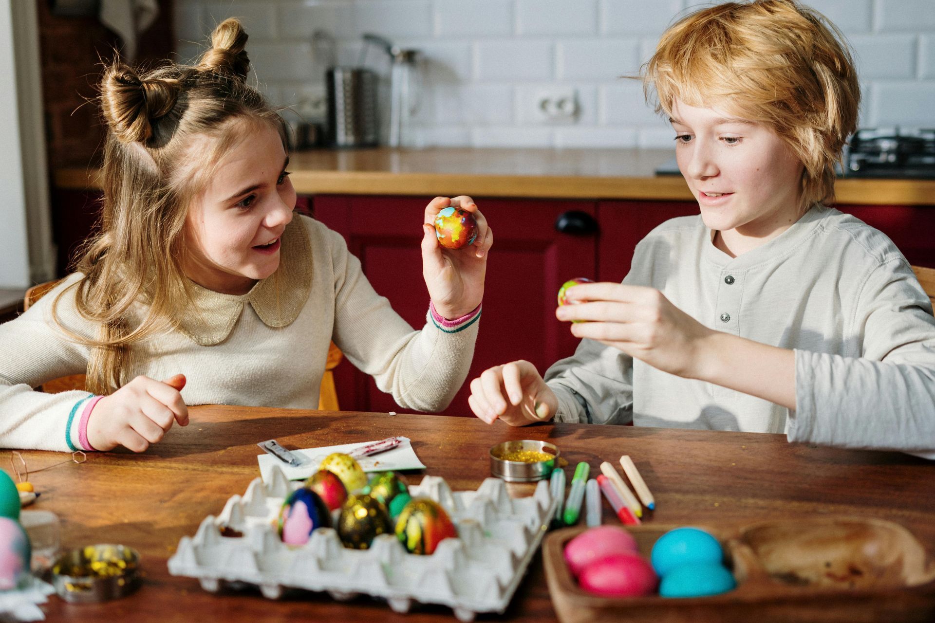 Two children are sitting at a table decorating Easter eggs