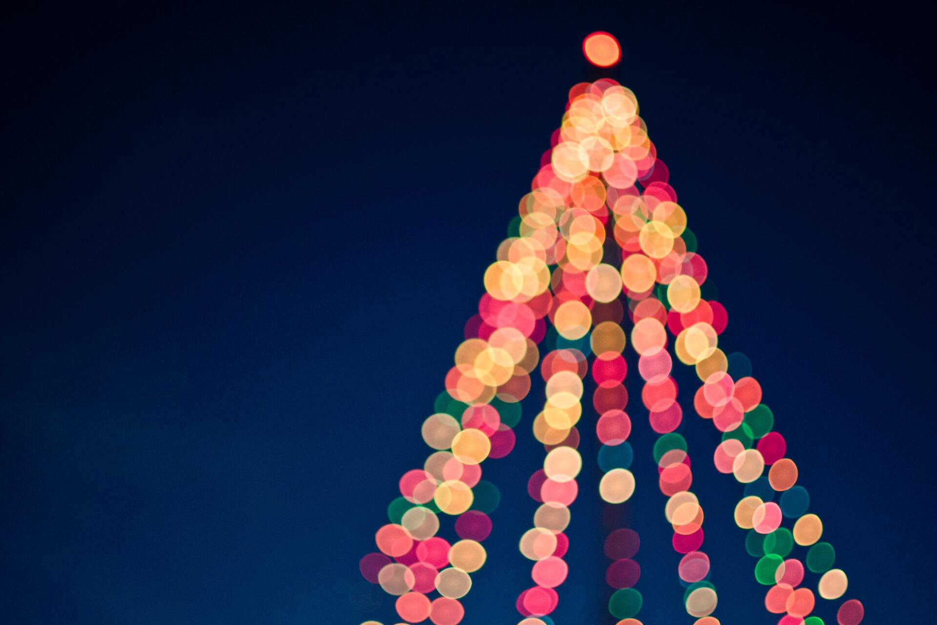 A bokeh effect on a photo of a large Christmas tree covered in lights.
