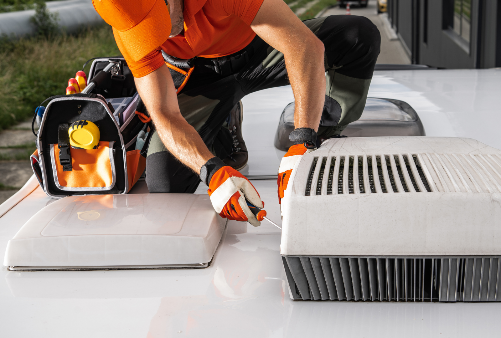 A person in work gear repairing rooftop AC units on a white surface. They are using a tool.