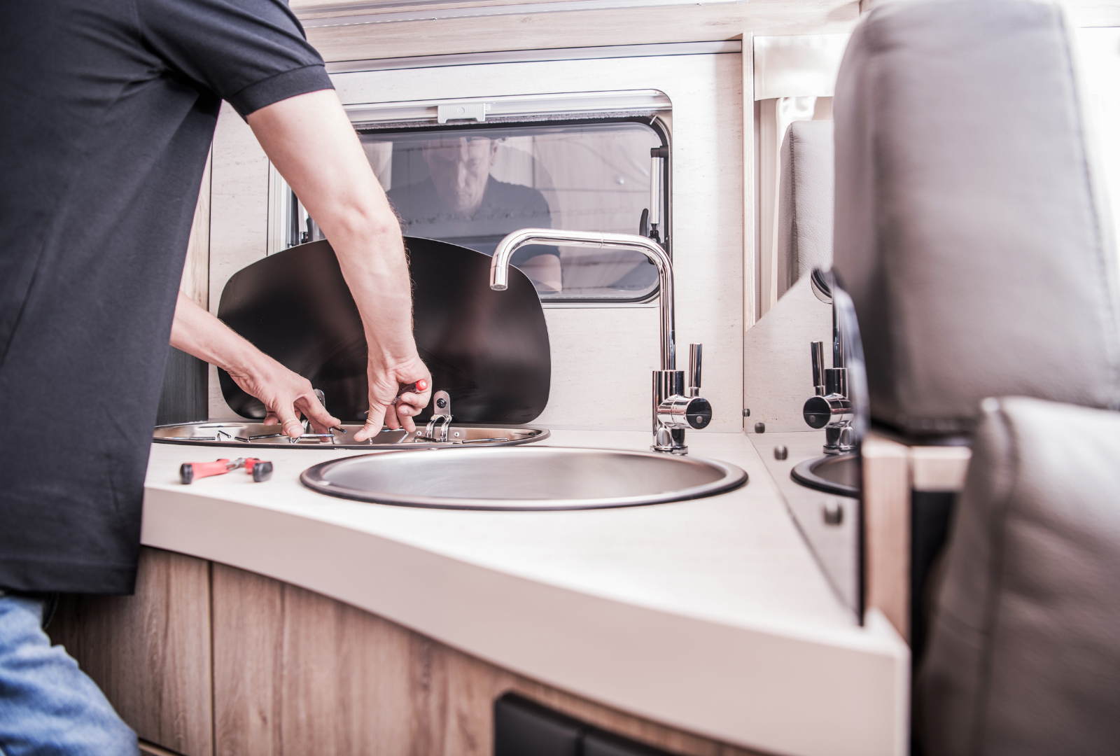 Person working on a sink in a motorhome. They are using tools to make a repair.