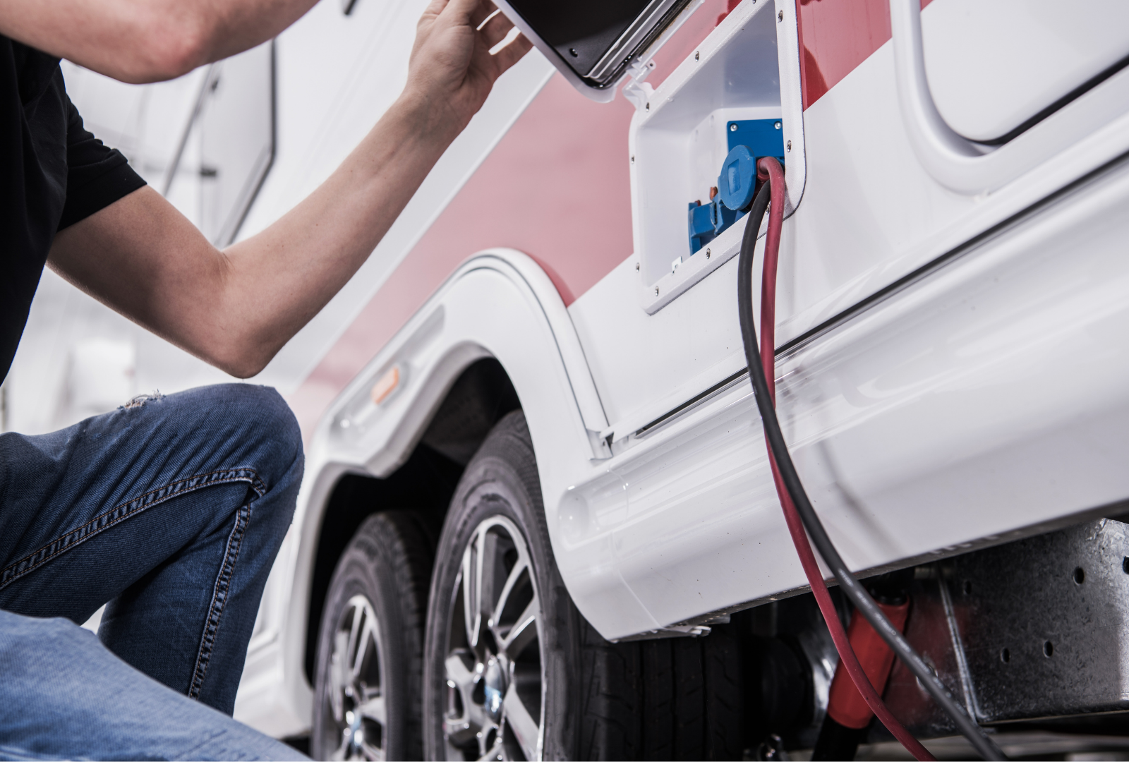 Person plugging a power cord into an RV. Black and red cables connected to a blue outlet.