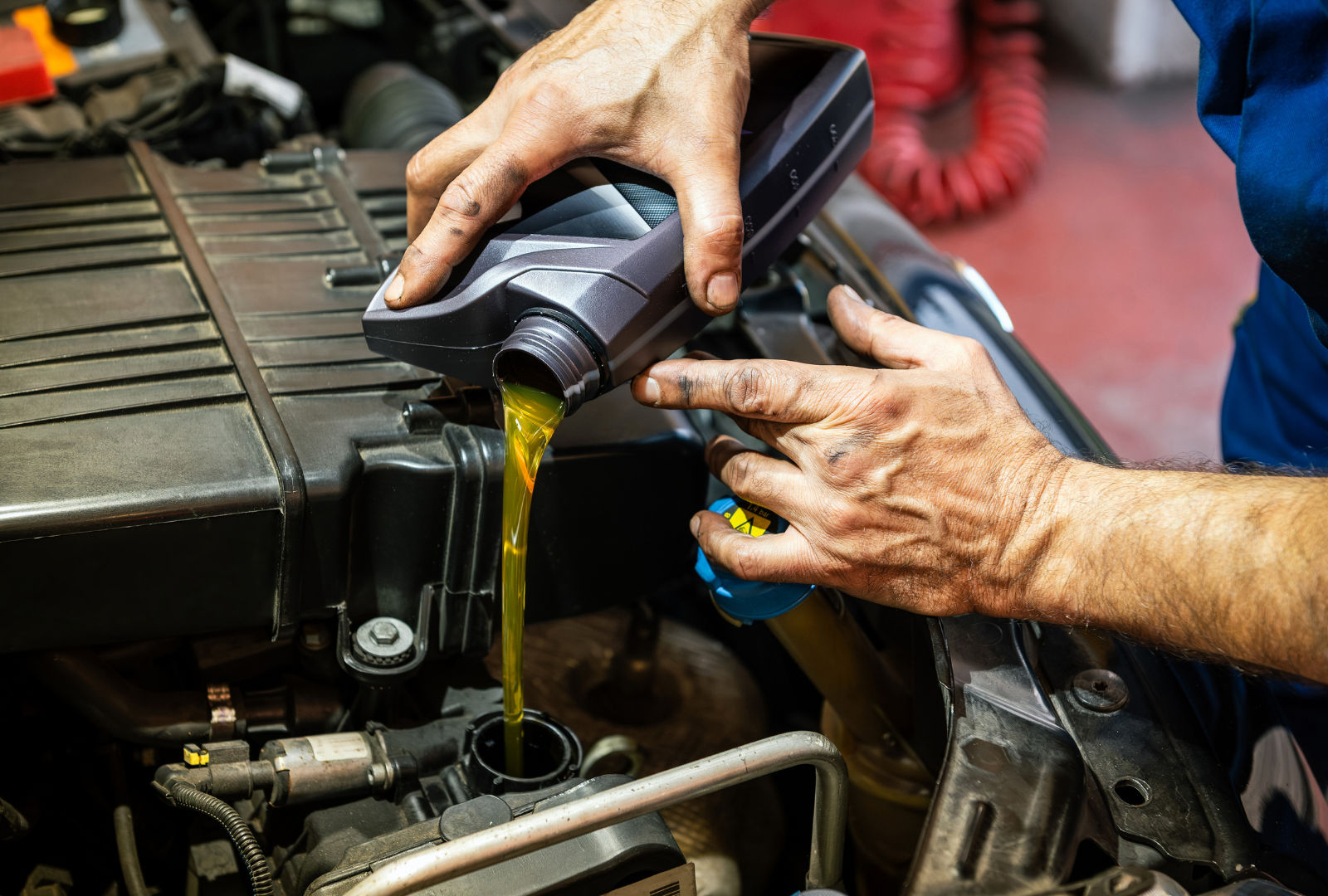 Mechanic pouring oil into a car engine, hands visible, in a garage.