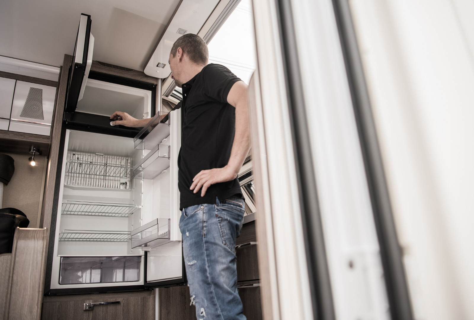 Man in jeans and black shirt looking in refrigerator in RV.