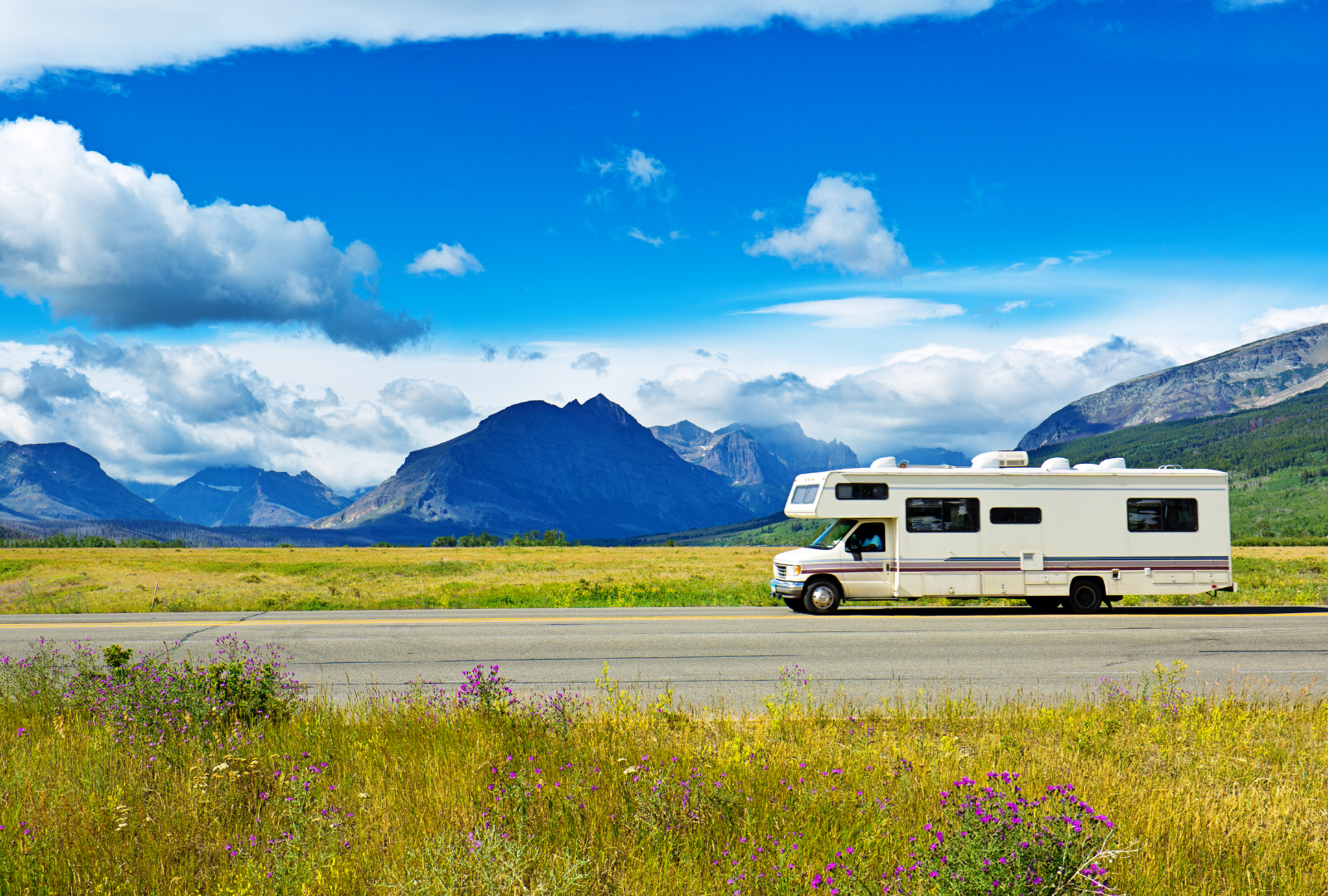 RV driving down a road with mountains and blue sky in the background.