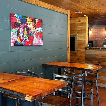 A restaurant with wooden tables and chairs and a painting on the wall above the tables.