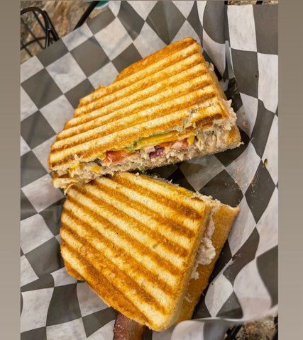 A panini sandwich is cut in half and sitting on a checkered paper.