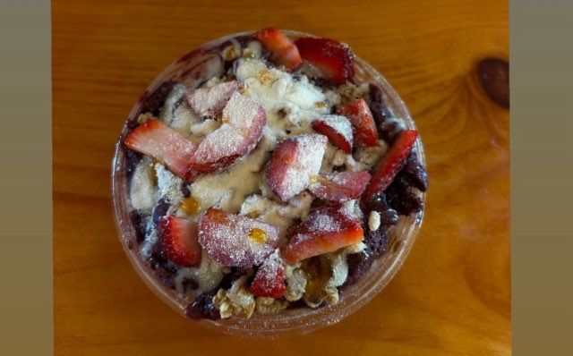 A bowl of food with strawberries and powdered sugar on a wooden table.
