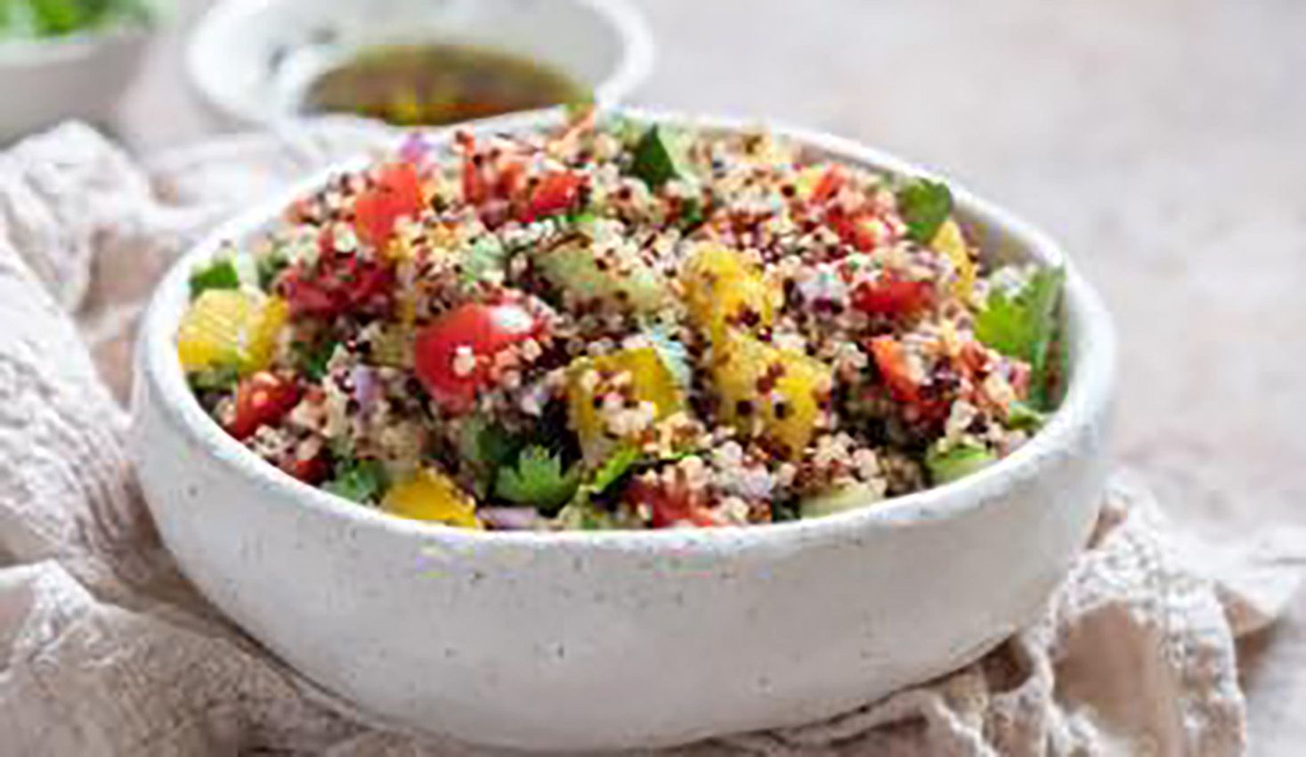 A white bowl filled with a salad of quinoa , tomatoes , cucumbers and other vegetables.