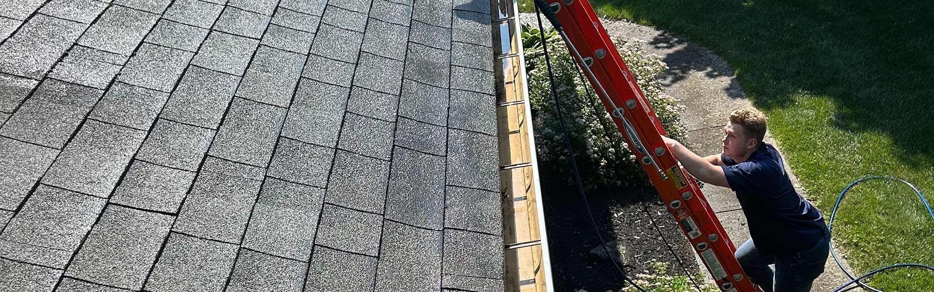 Person climbing a red ladder next to a roof covered with gray shingles