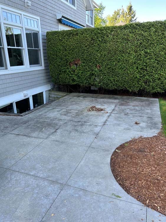 Gray concrete patio next to a building with a green hedge and mulched area