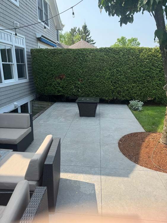 Backyard patio with concrete flooring, seating, fire pit, and hedge.