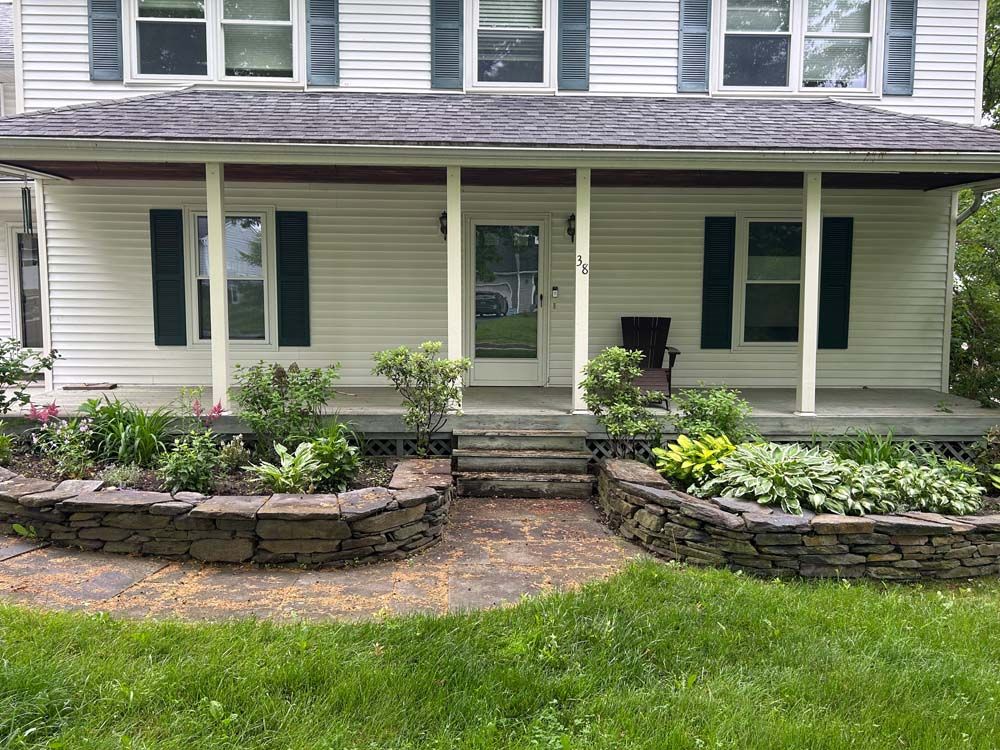 White house with a porch, stone flower beds, and green lawn