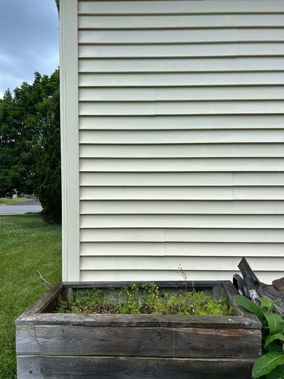 Wooden planter box with greenery beside a cream-colored house