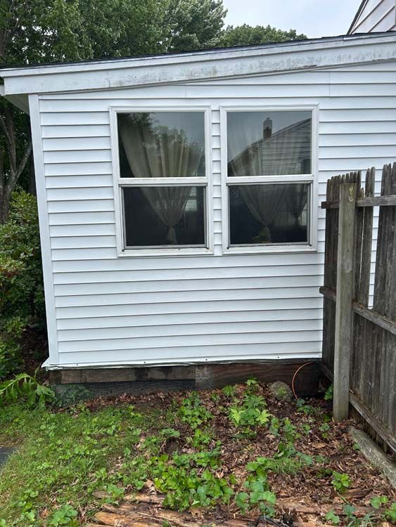 White-sided building with two windows and a small garden, viewed outdoors