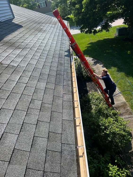 Person on ladder cleaning out a gutter on a roof