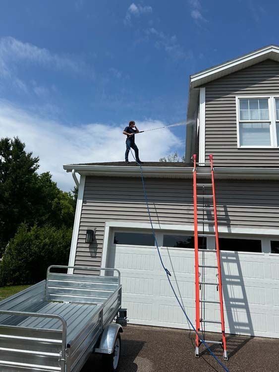 Person pressure washing a house's upper siding from a roof