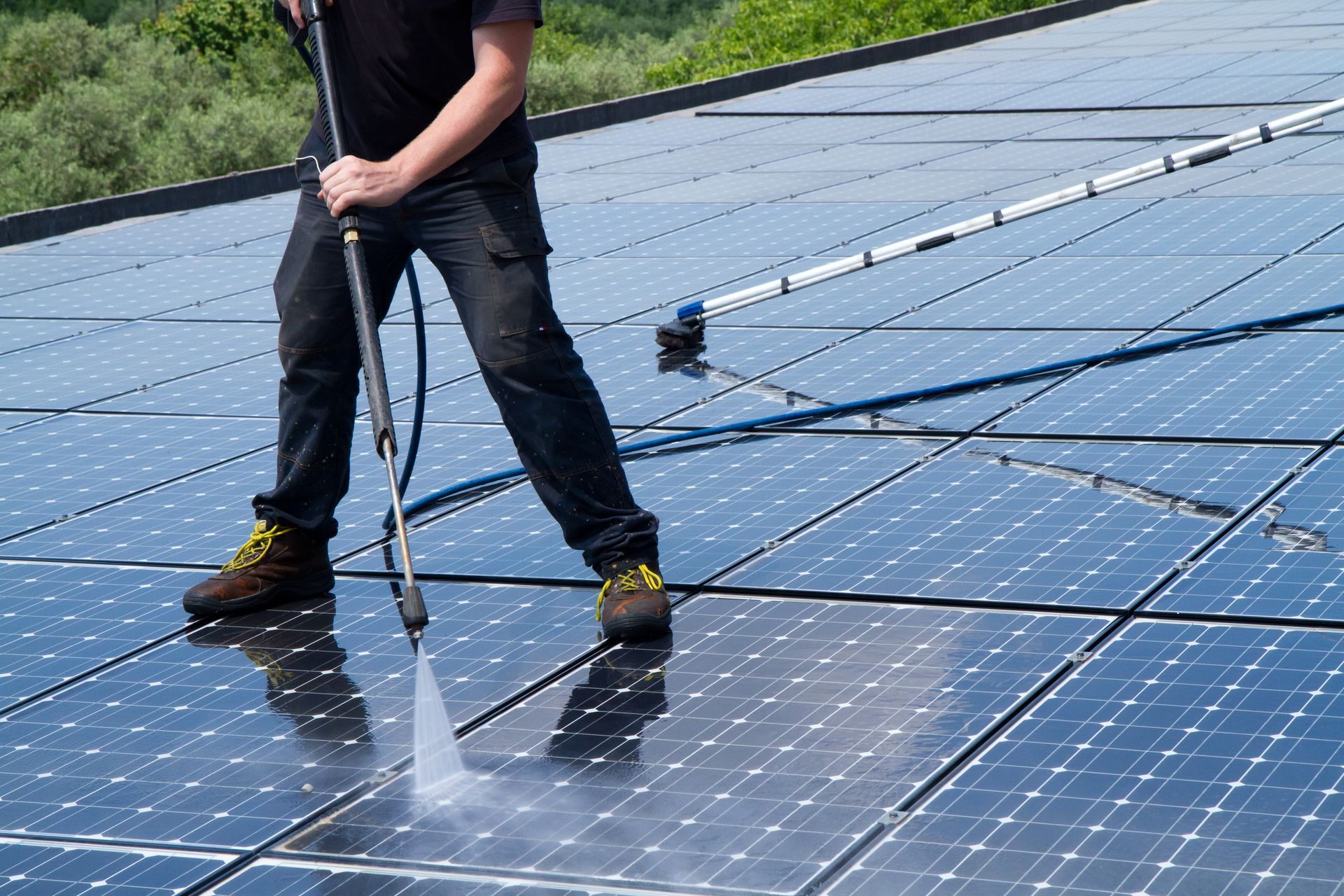 Person cleaning solar panels with a pressure washer on a rooftop