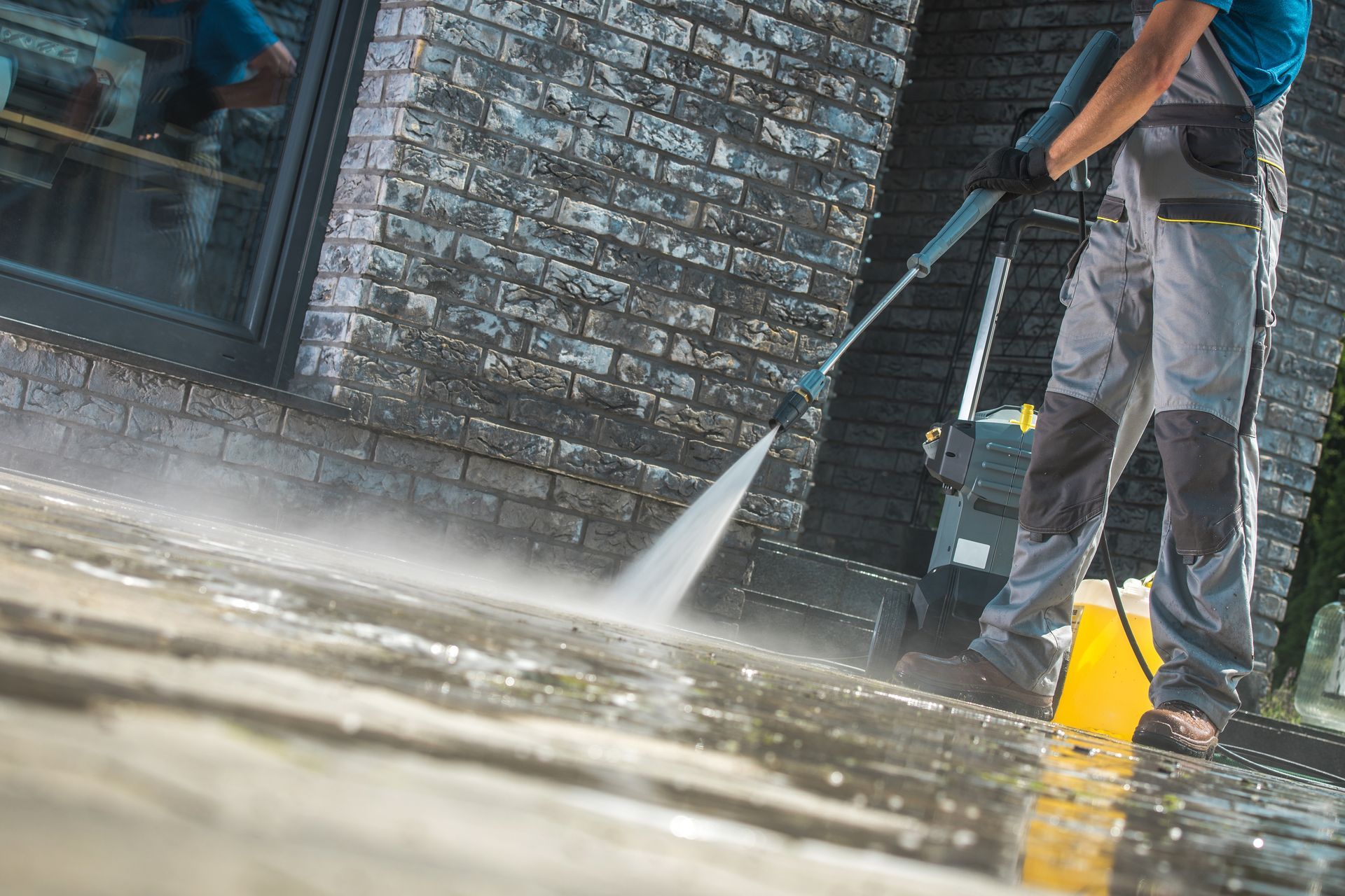Person power washing a brick wall and paved surface with a high-pressure washer