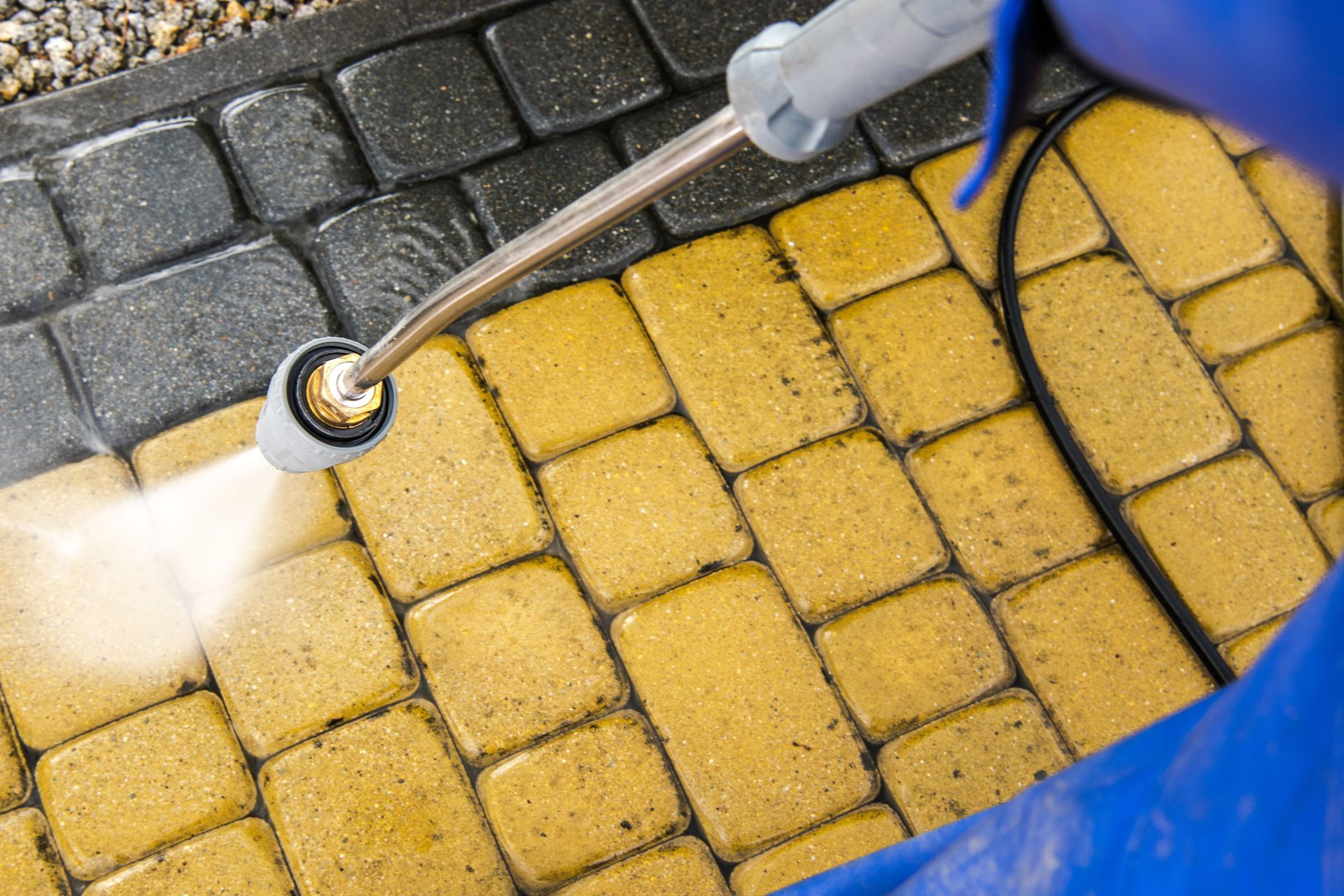 Pressure washer cleaning yellow and black patio pavers