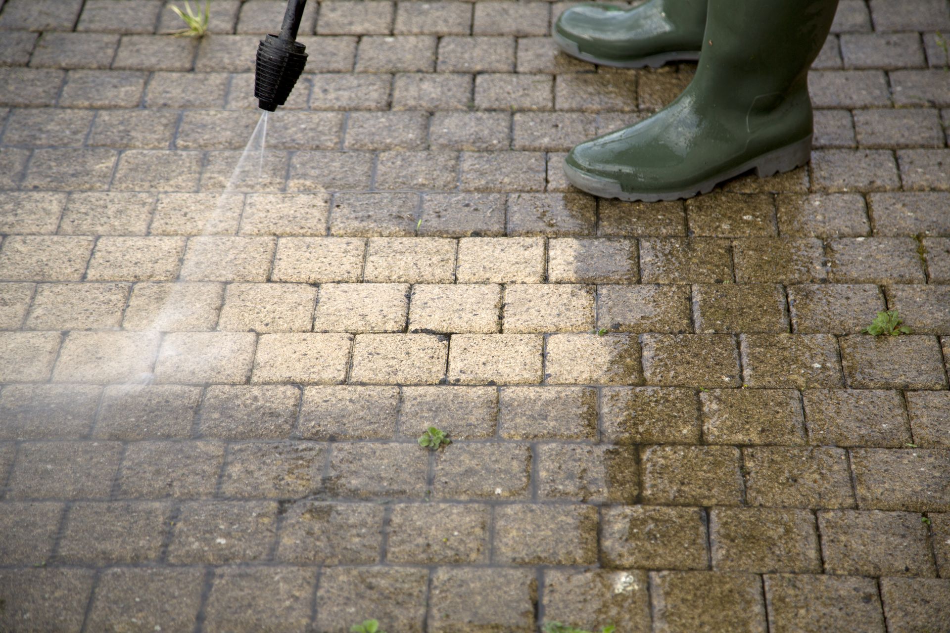 Pressure washing brick pavers with green boots visible