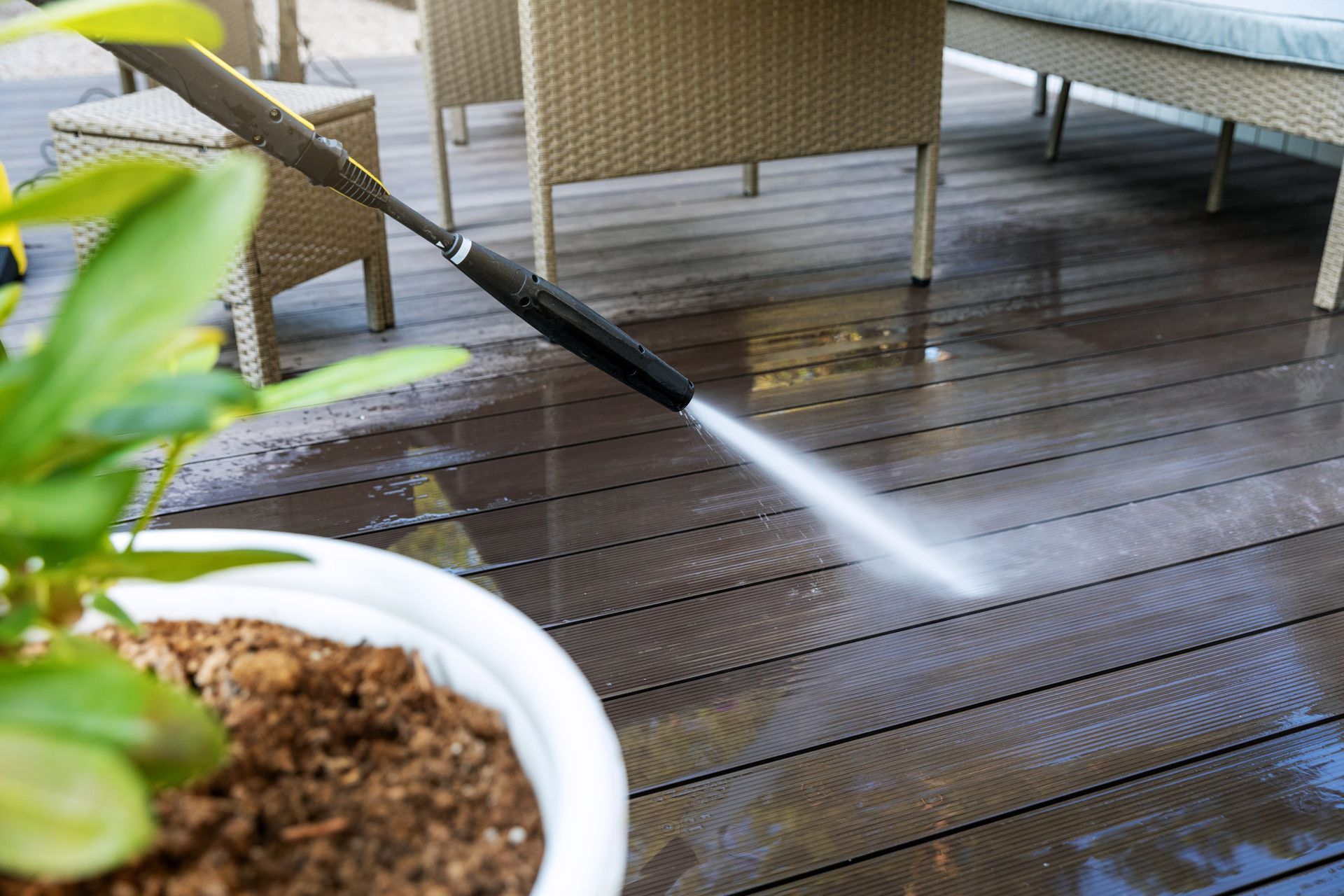 Pressure washer spraying water on a wooden deck; patio furniture in the background