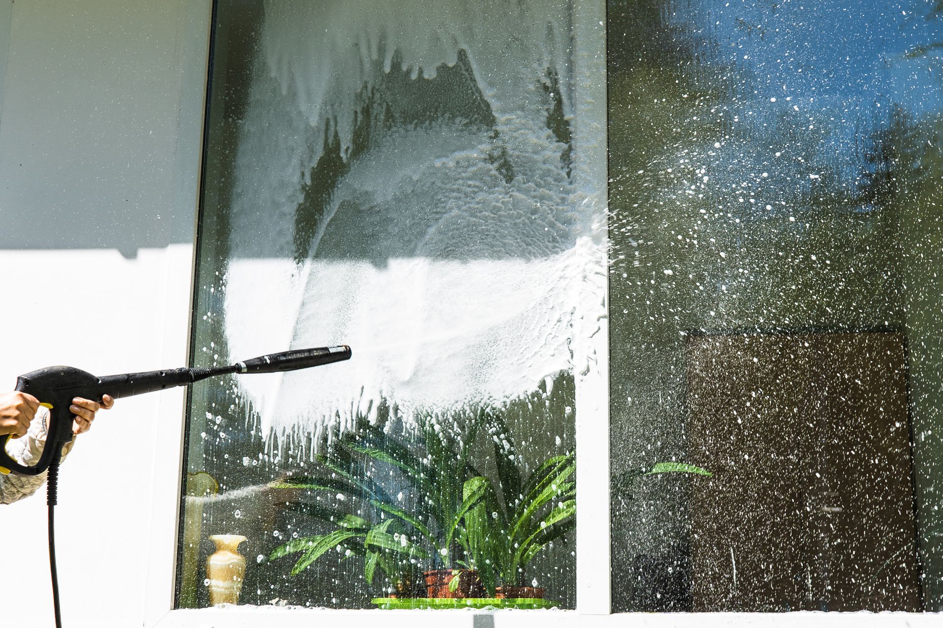 Person using a pressure washer to clean a window