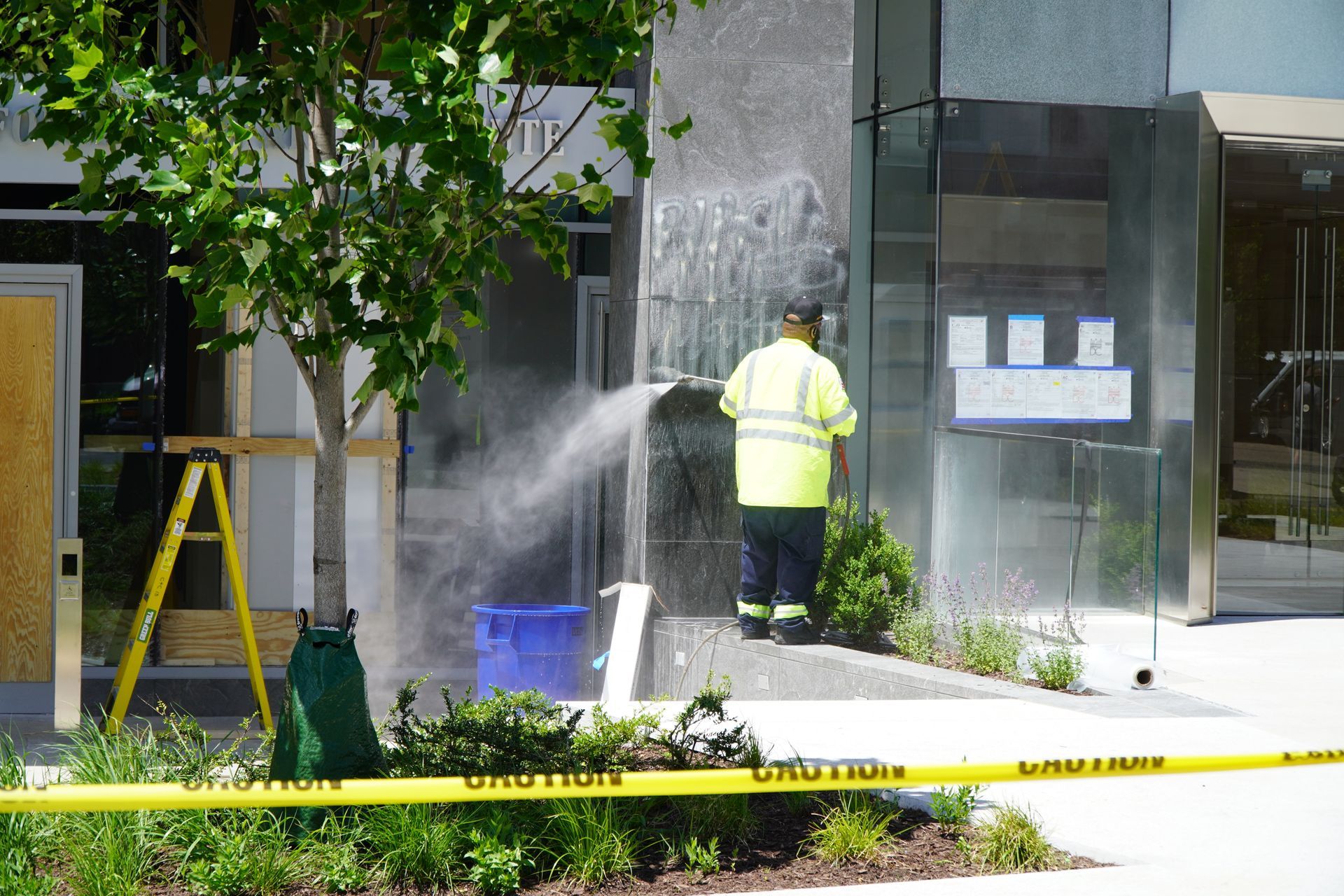 A person in a yellow vest sprays a water feature next to a building