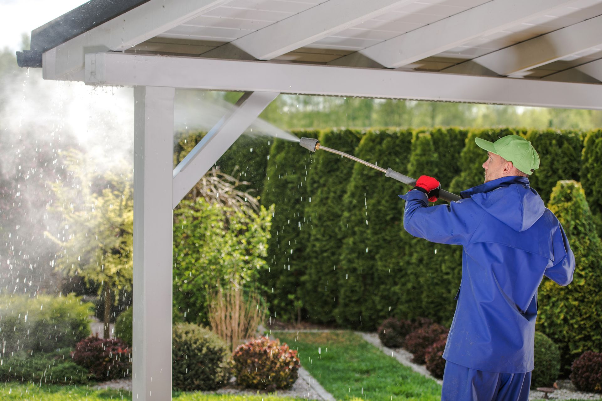 Man power washing a white pergola with a water hose in a garden setting