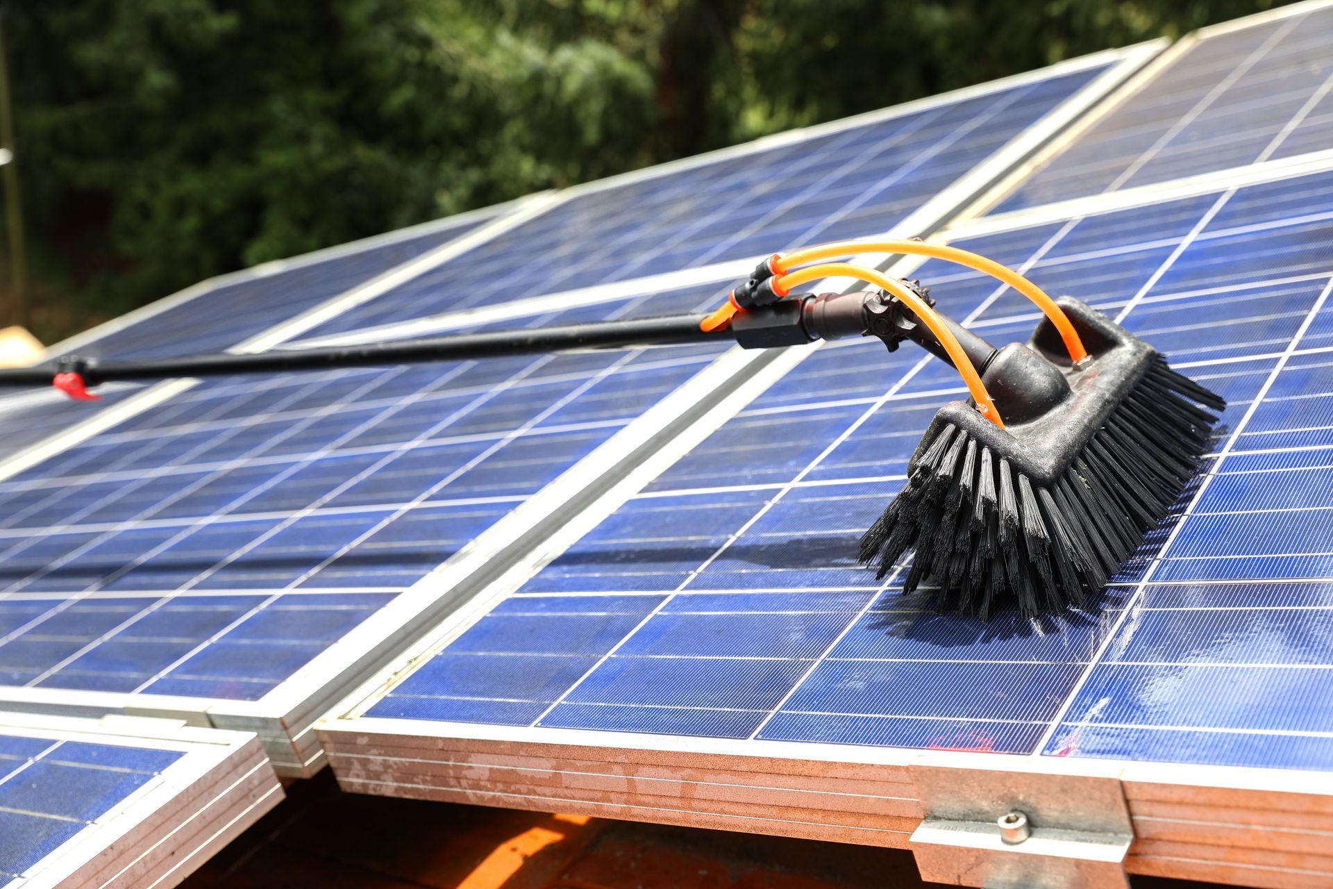 Solar panel being cleaned with a brush attached to a long handle