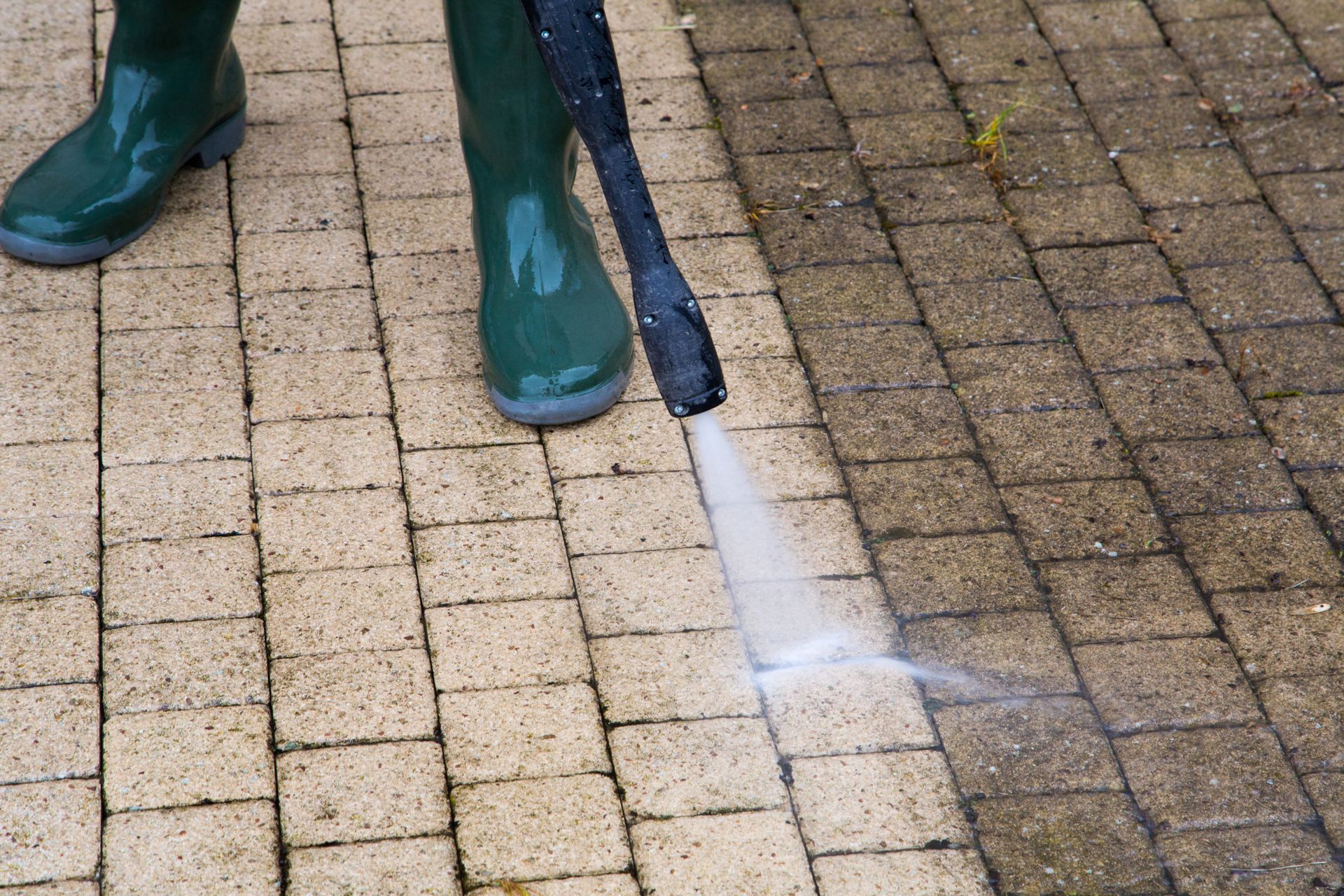 Person in green boots pressure washing a brick walkway
