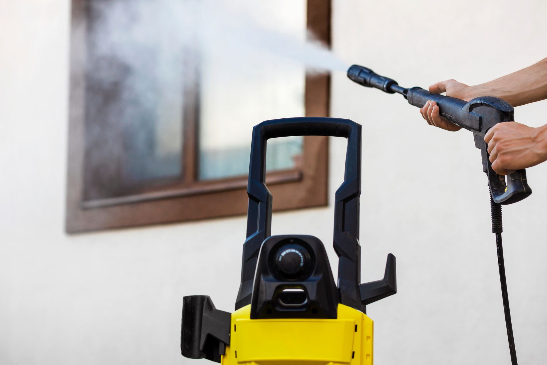 Person power washing a window with a yellow and black pressure washer