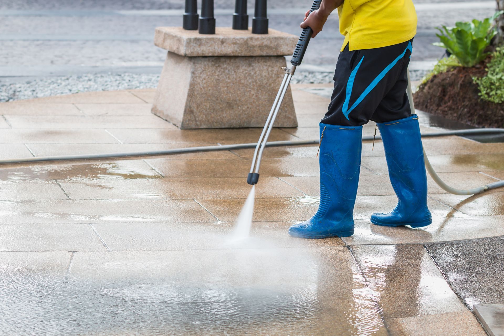 Person wearing blue boots pressure washing a wet