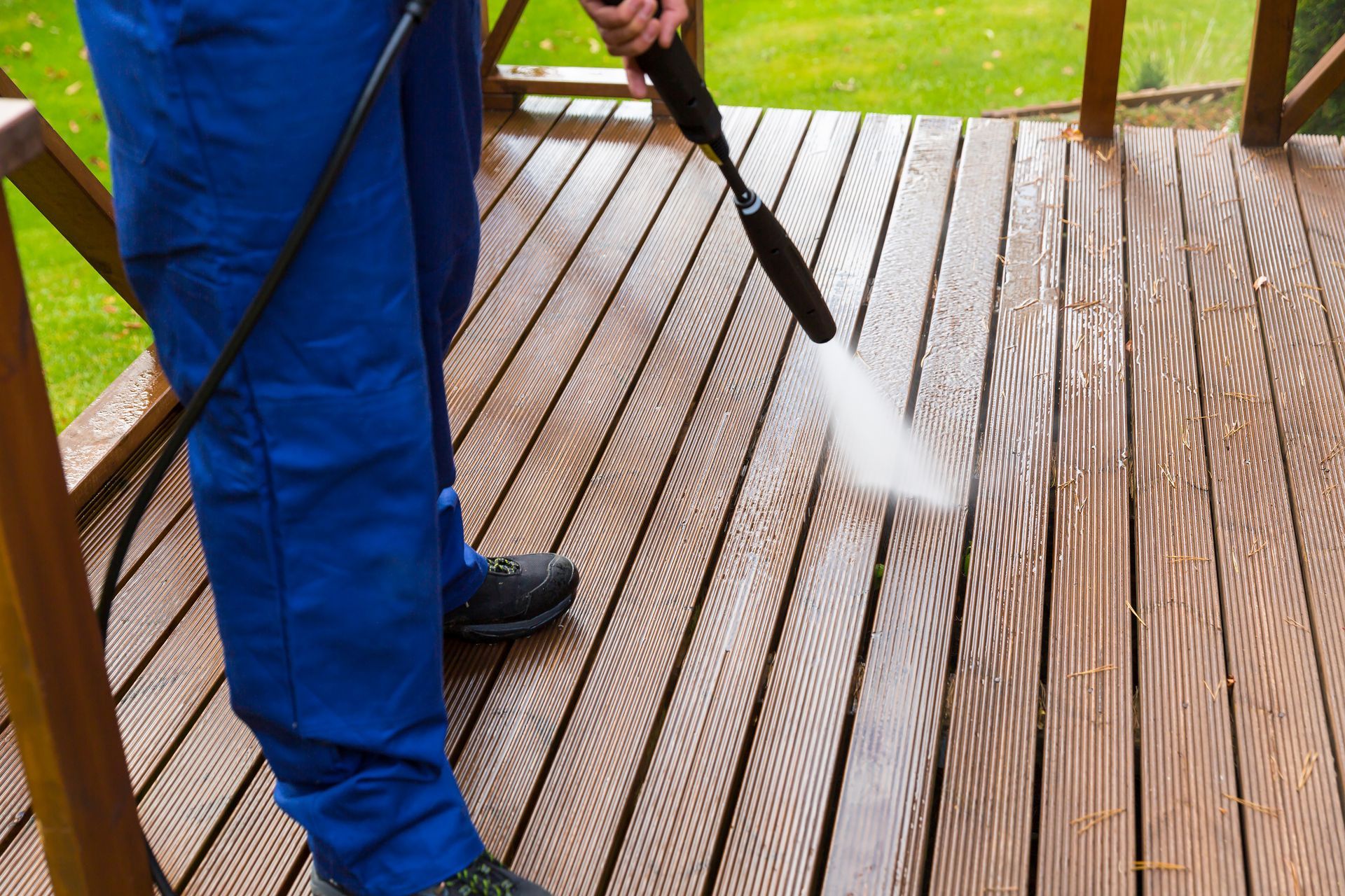 Person pressure washing a wooden deck