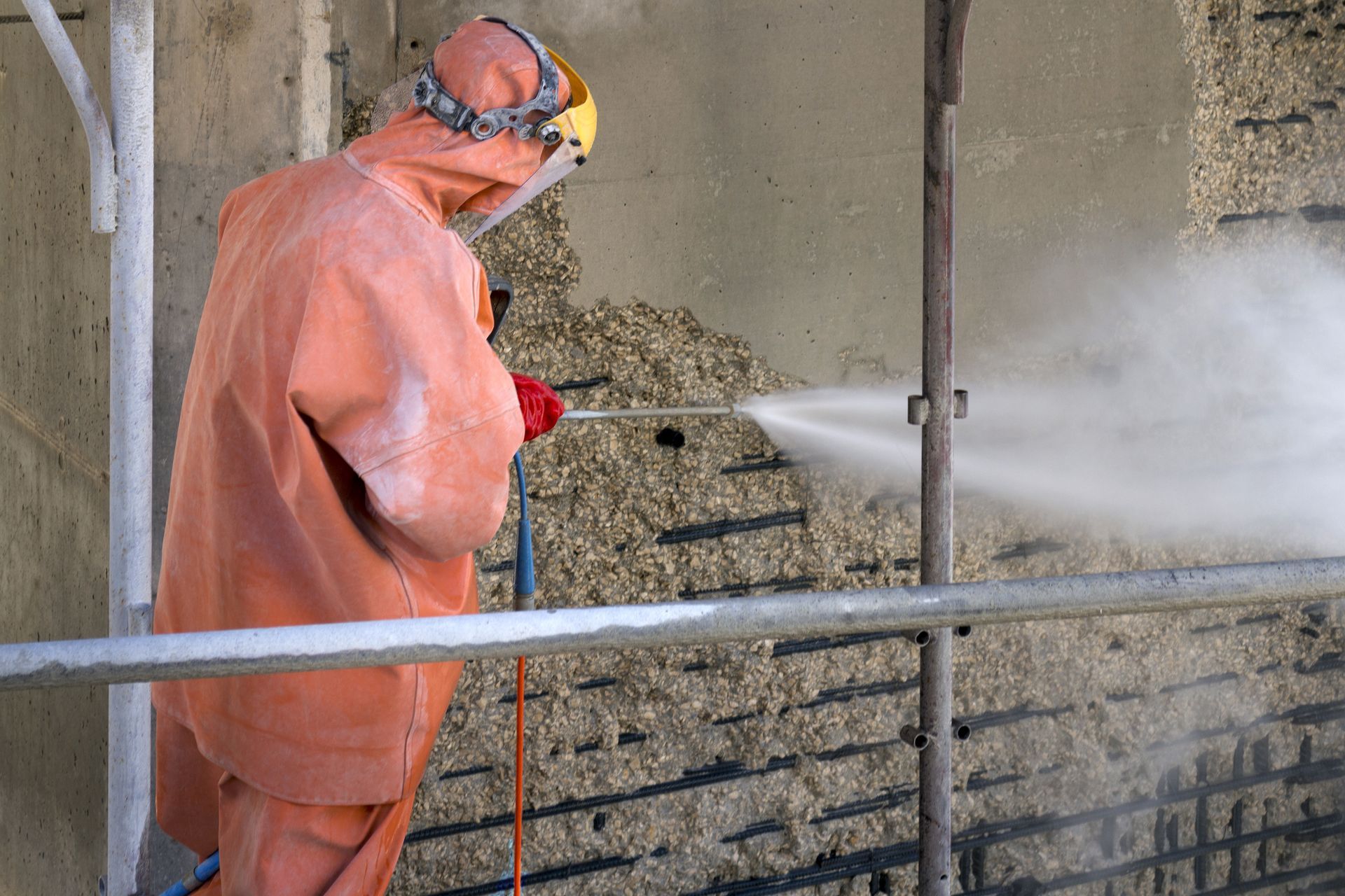 Worker in protective suit blasting concrete wall with water